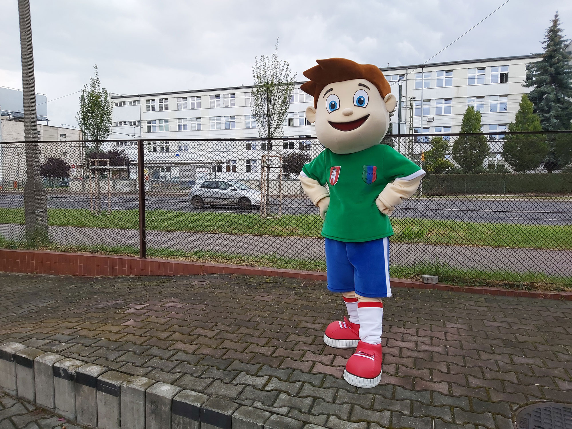 Na fotografii widnieje strój reklamowy w postaci chłopca stylizowanego na postać piłkarza pozujący do zdjęcia przed siedzibą firmy Elabika